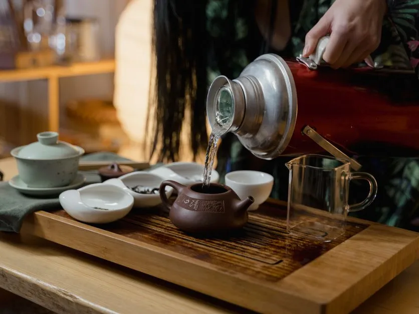 Eau chaude versée dans une théière en céramique sur une planche en bois